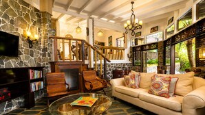 A cozy living room with a stone wall, wooden furniture, a glass coffee table, and a beige sofa with patterned cushions. - 3 bedroom Villa with Pool + Ocean Views - Overlooks Golf course (Gros Islet)