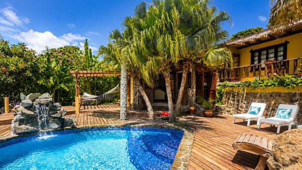A pool with a waterfall, surrounded by wooden decking, palm trees, and lounge chairs. - 3 bedroom Villa with Pool + Ocean Views - Overlooks Golf course (Gros Islet)