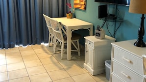 Une pièce comprenant une table à manger, des chaises, un téléviseur, une lampe et un petit meuble.