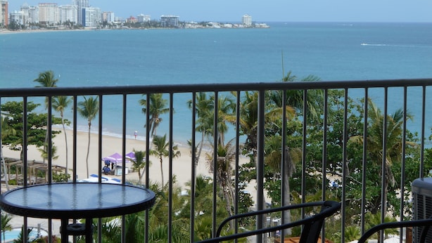 Un balcon avec vue sur une plage et sur les bâtiments d’une ville.