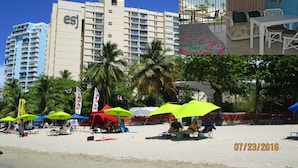 Un hôtel doté d’un balcon donnant sur une plage, d’un espace repas avec vue et d’une zone de plage équipée de parasols et de chaises longues.