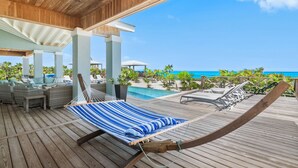 Une terrasse en bois avec un hamac, des chaises longues et une piscine.