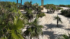 Un belvédère doté d’un toit en tuiles, offrant une vue sur une plage aux eaux bleu azur et bordée de palmiers.