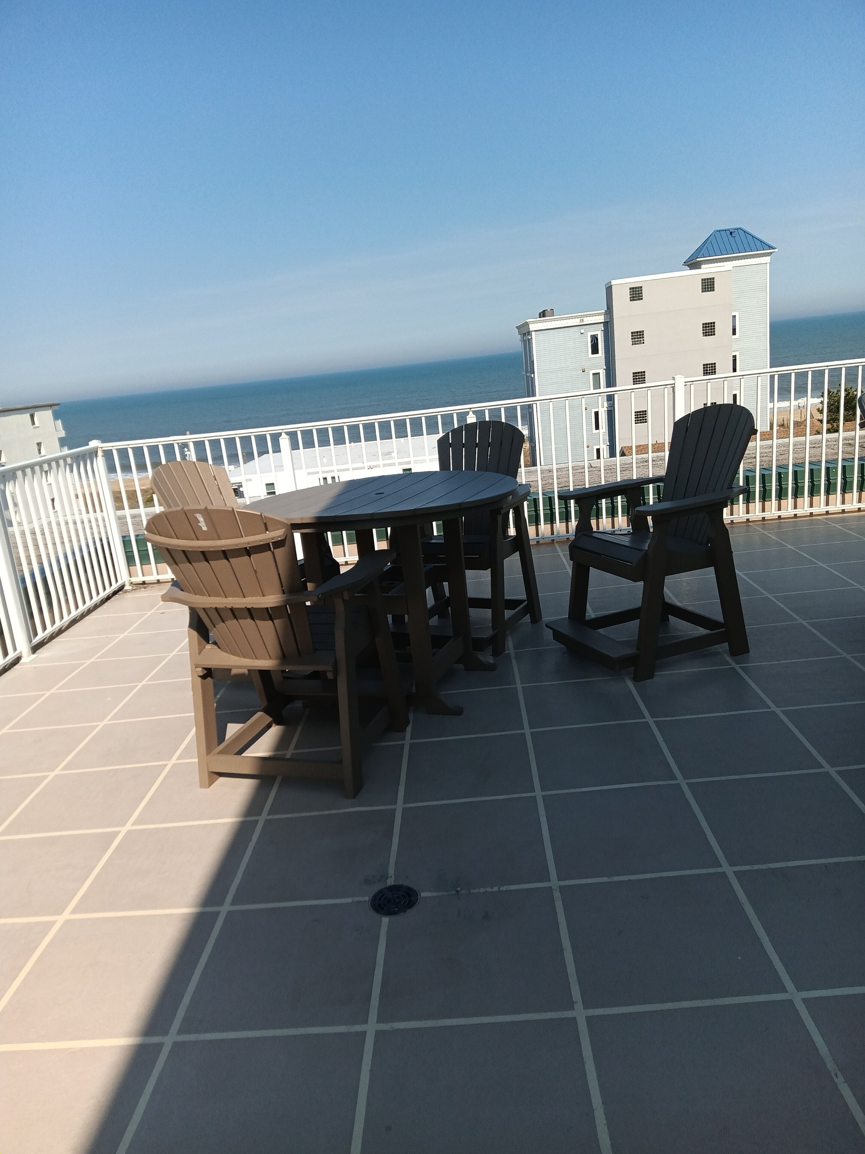 A terrace with a table and chairs, a view of the ocean, and a building in the background.