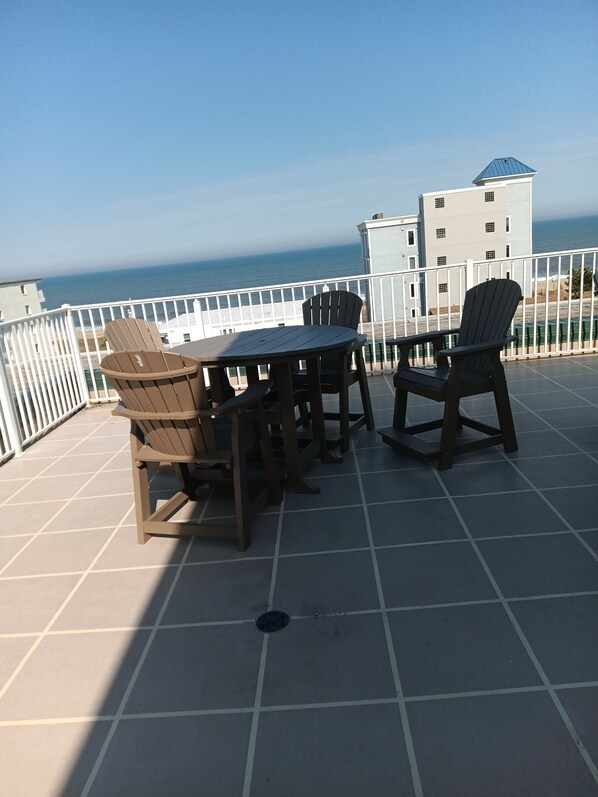 A terrace with a table and chairs, a view of the ocean, and a building in the background. - Ocean Block-Crib, stroller, high chair included, great for extended families! (Ocean City)