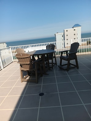 A terrace with a table and chairs, a view of the ocean, and a building in the background. - Ocean Block-Crib, stroller, high chair included, great for extended families! (Ocean City)