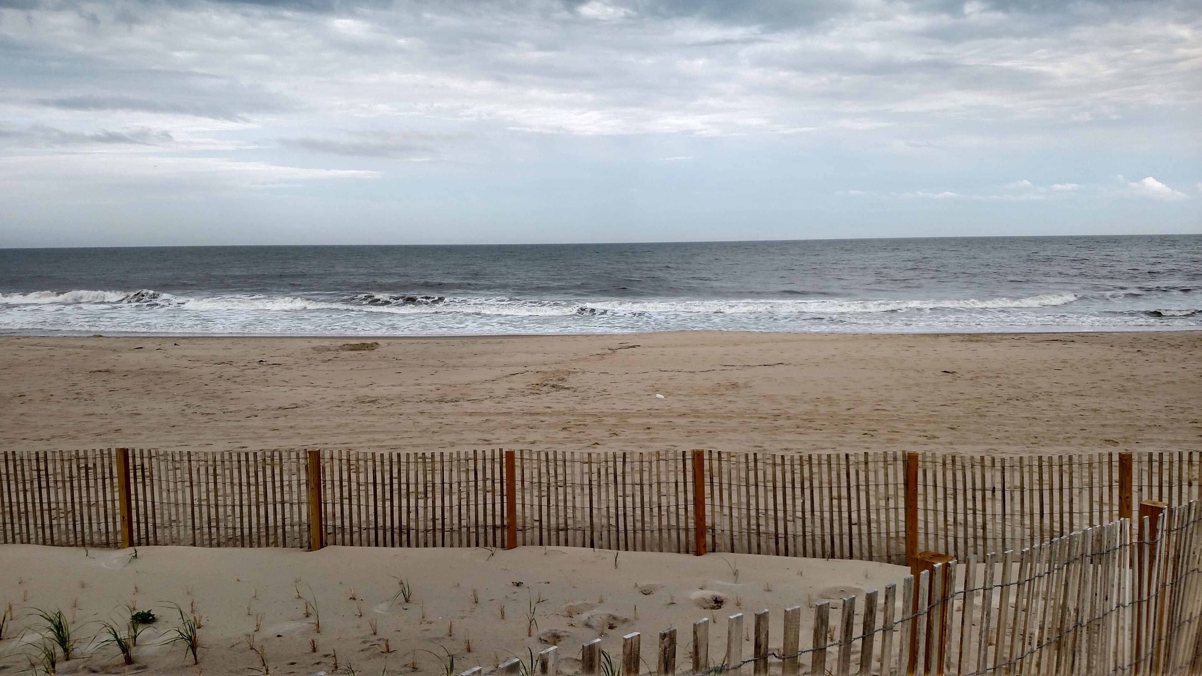 Une plage avec une clôture en bois au premier plan et l’océan en arrière-plan.