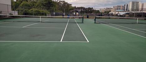 A tennis court with a net in the center, surrounded by a fence.