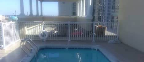Una piscina con una escalera metálica y una zona de estar cubierta.