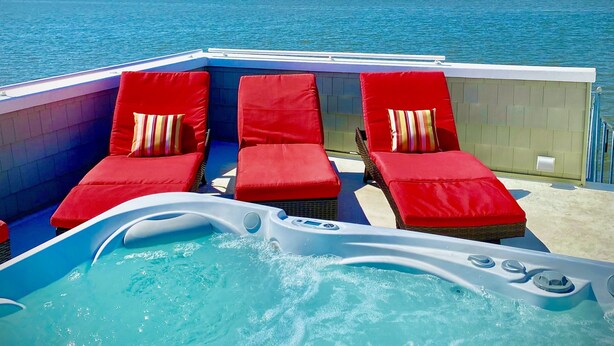 A pool area with red lounge chairs and a hot tub on a boat.