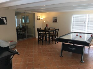 A room with a pool table, a dining table with chairs, a sofa, and a sliding glass door leading to a dining area.