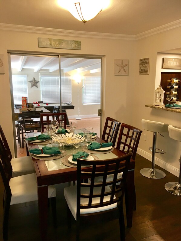 A dining area with a wooden table set for six, chairs, and a bar area with a white bar stool.