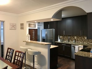 A modern kitchen with dark cabinetry, a granite countertop, and a built-in island with bar stools.