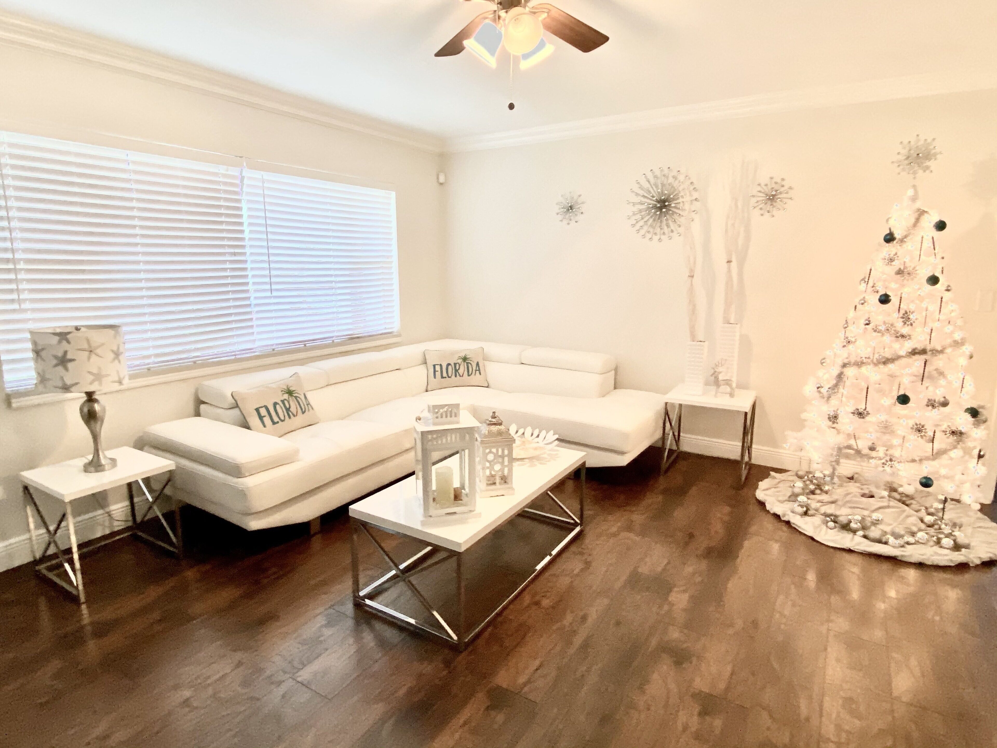 A modern living room with a white sectional sofa, a glass coffee table, and a white Christmas tree.