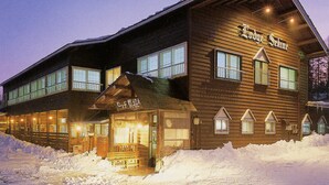 A wooden lodge with a large entrance and multiple windows, surrounded by snow. - Park Lodge Sekine (Myoko)