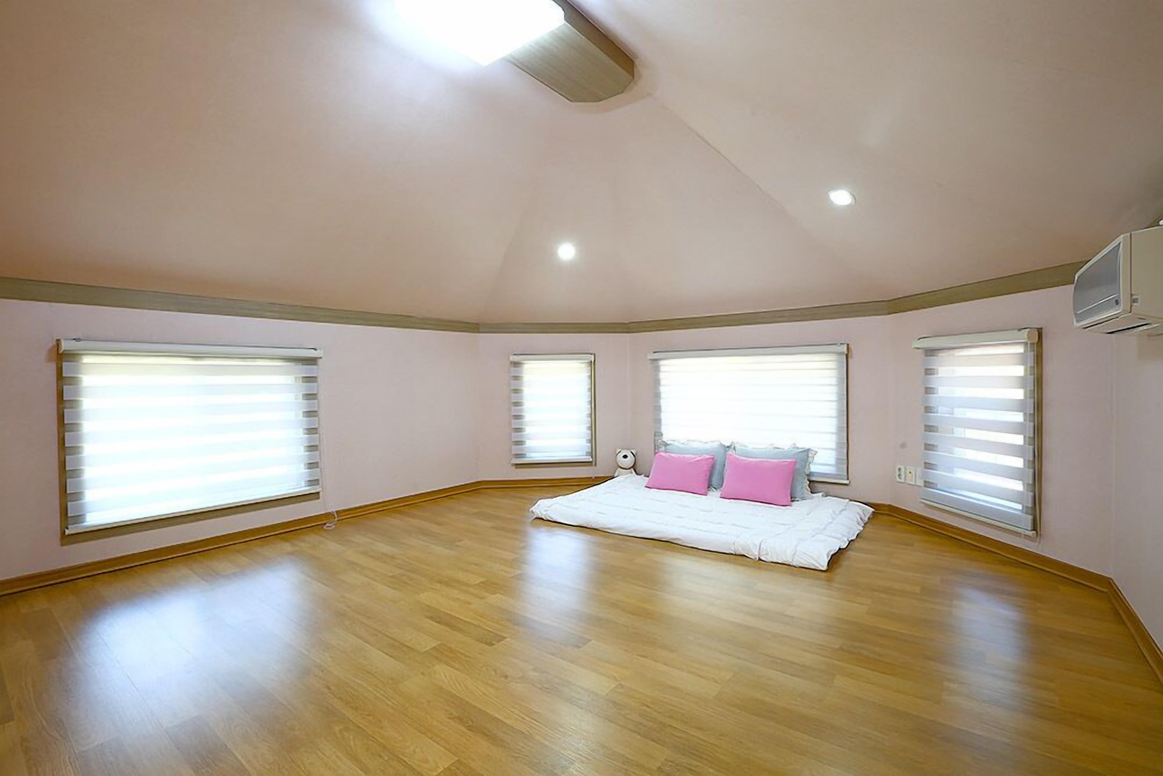 A spacious room with large windows, a ceiling fan, and a bed with pillows.
