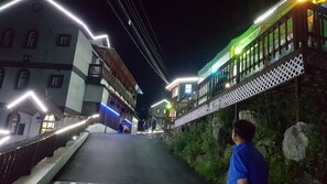A narrow street with buildings on either side, a pedestrian bridge, and a person standing on the bridge. - Haena Pension (Gapyeong)