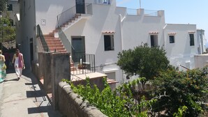 Ein zweigeschossiges Gebäude mit Treppe, Balkon und einem Garten mit orangefarbenen Blüten.
