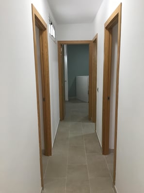 A narrow hallway with wooden doors on either side, leading to a room with a blue wall and a white door.