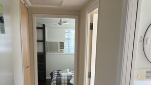 A narrow hallway with a bed in the background, a ceiling fan, and an air conditioning unit.