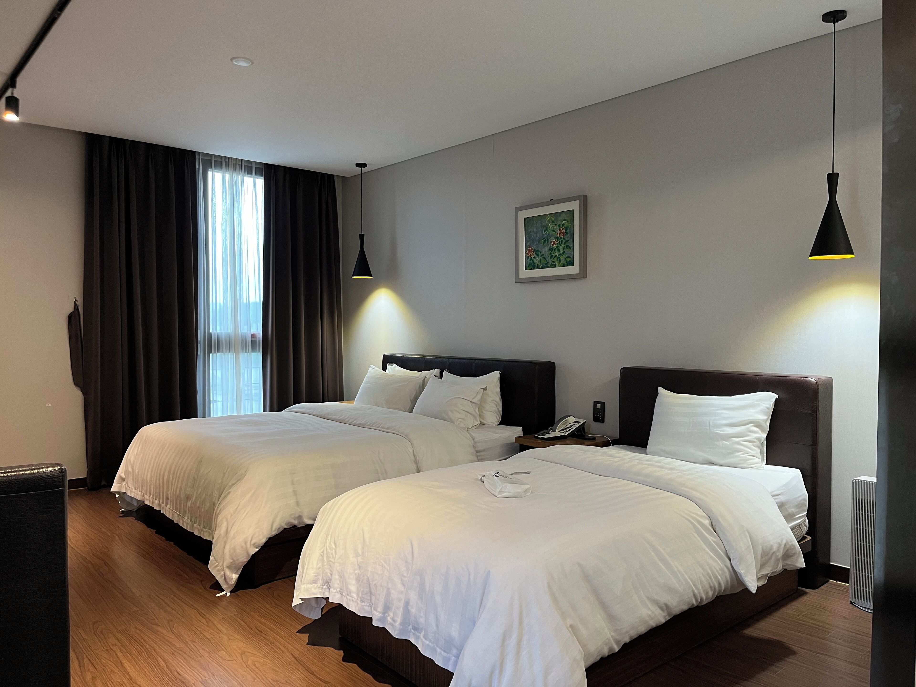 Una camera d'albergo con due letti, un'ampia finestra con tende, un quadro al muro e un telefono sul comodino.