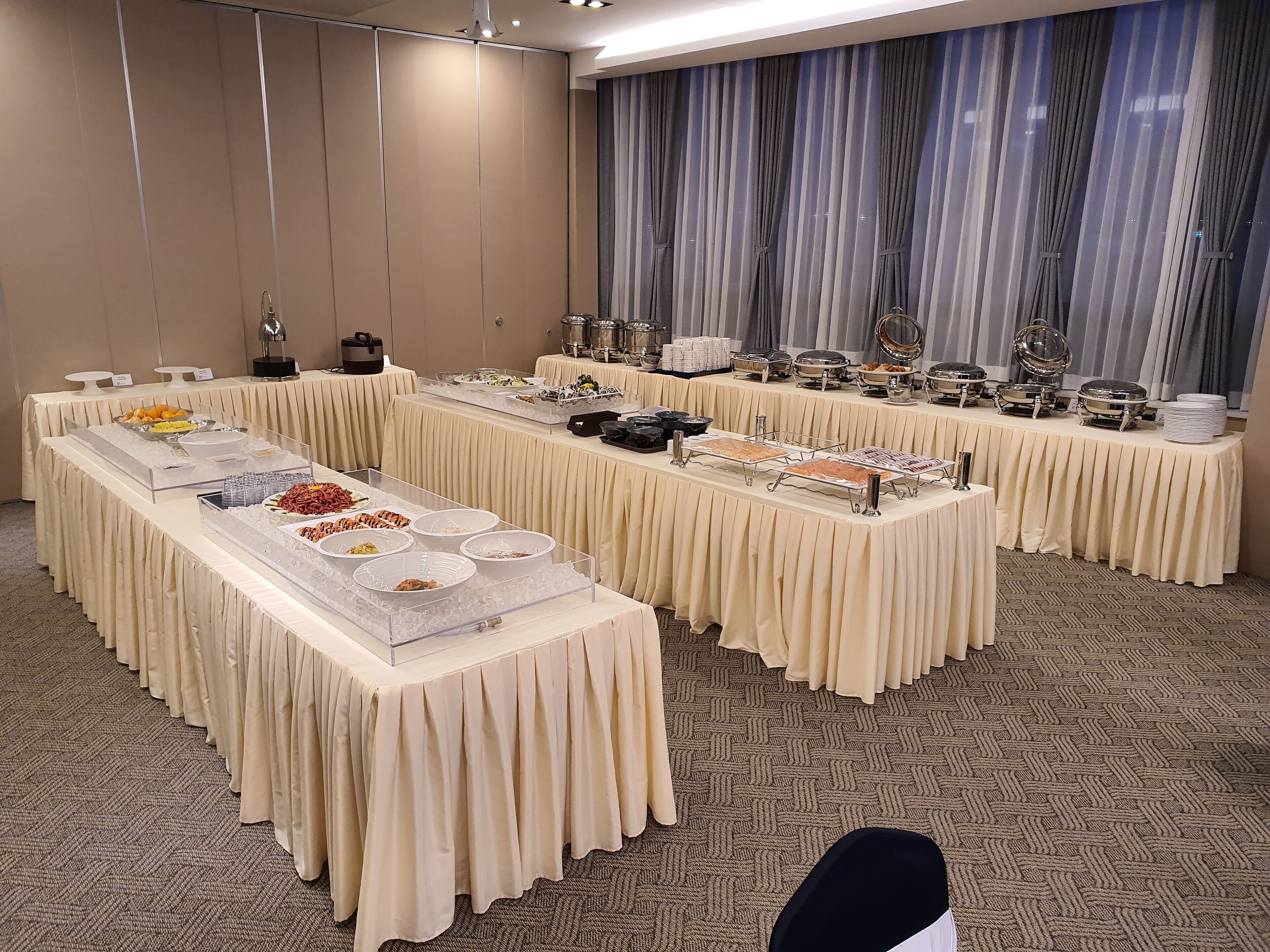 A buffet setup with multiple tables covered in beige tablecloths, featuring various food items and serving dishes.