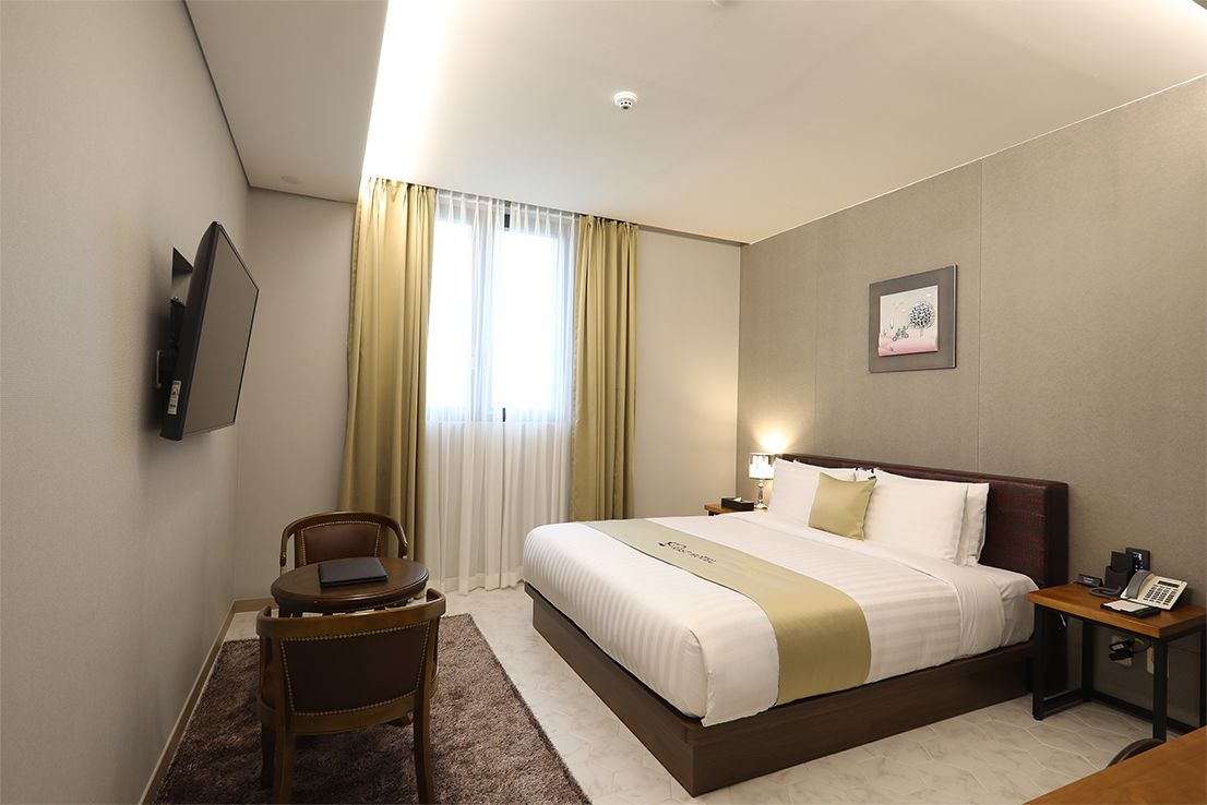 A hotel room with a bed, a desk, a chair, a TV, and a window with curtains.