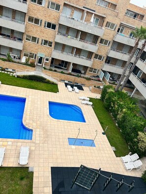 Un edifici residencial de diverses plantes amb piscina, zona de seients a l'aire lliure i jardí ben cuidat.
