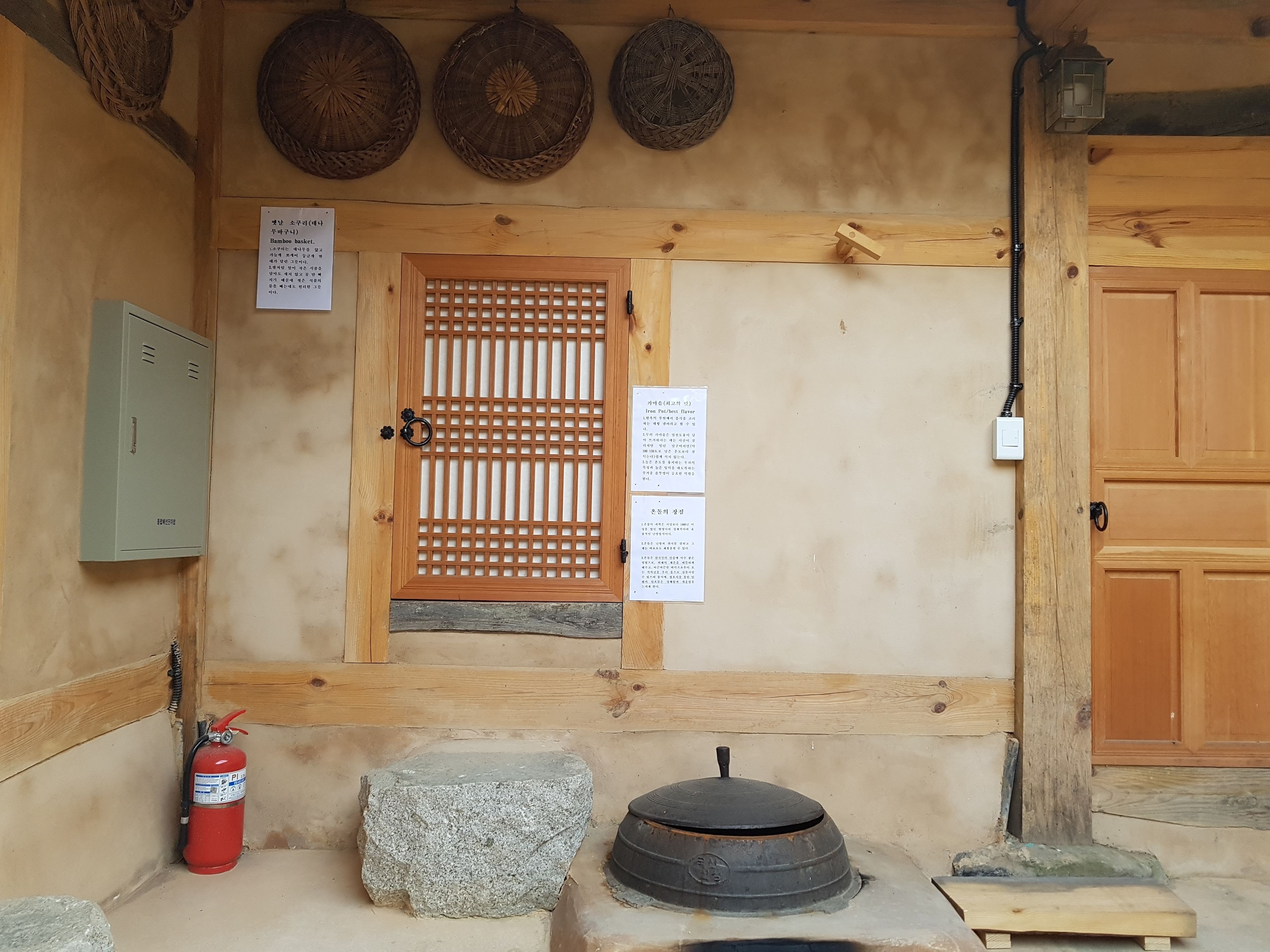 Une porte en bois ornée d’un motif quadrillé, un extincteur, un bloc de pierre et un poêle traditionnel.