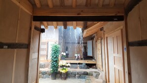 A wooden interior with a stone pathway leading to an outdoor area with a water feature and potted plants. - Jukheon Traditional House (Andong)