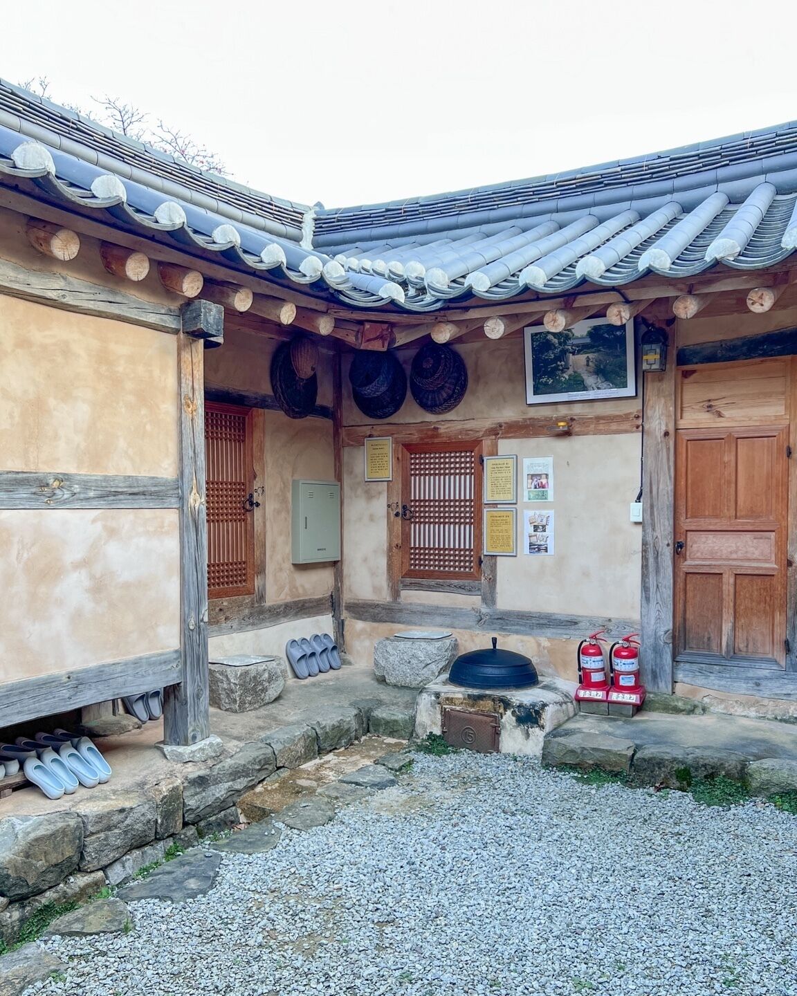 A traditional Korean hanok with a tiled roof, wooden doors, and a small courtyard with stone steps and fire extinguishers.
