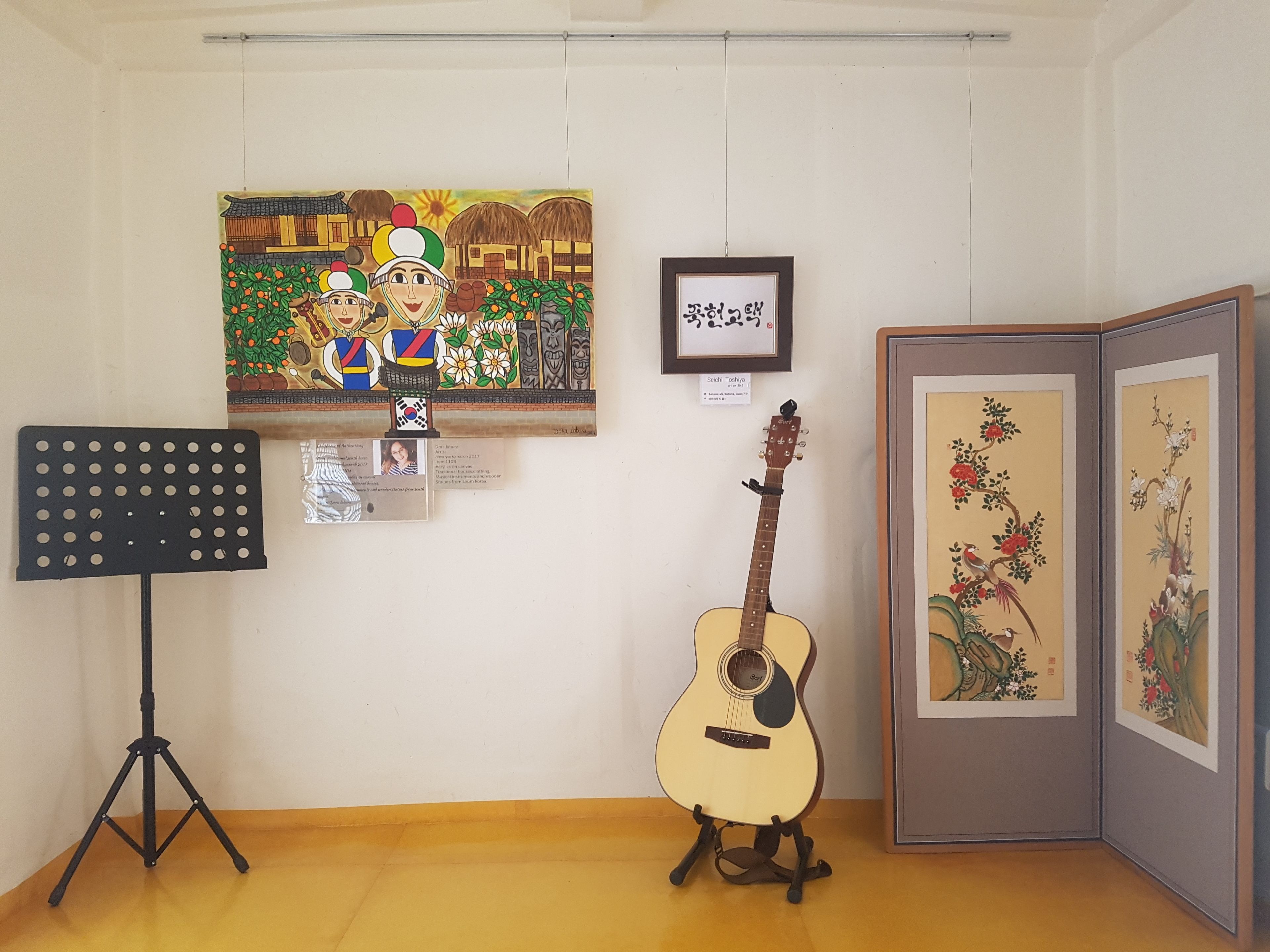 Una habitación con una guitarra sobre un atril, un caballete para música y cuadros en la pared.