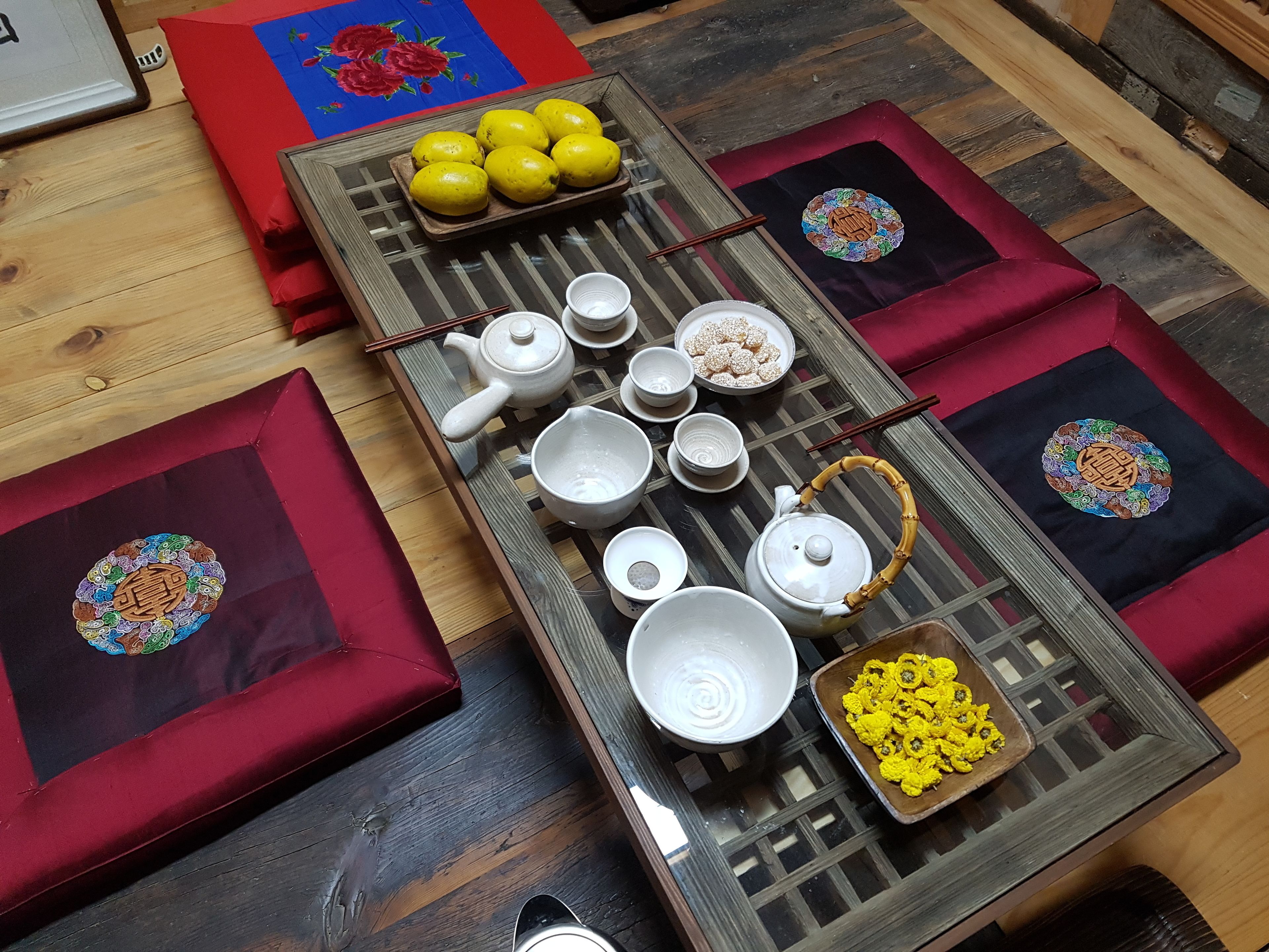 A dining table with various dishes, including a teapot, cups, and a bowl of yellow flowers.