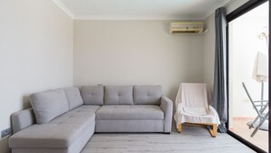 En moderne stue med en grå hjørnesofa, en hvid lænestol og en stor skydedør til et udendørs område.