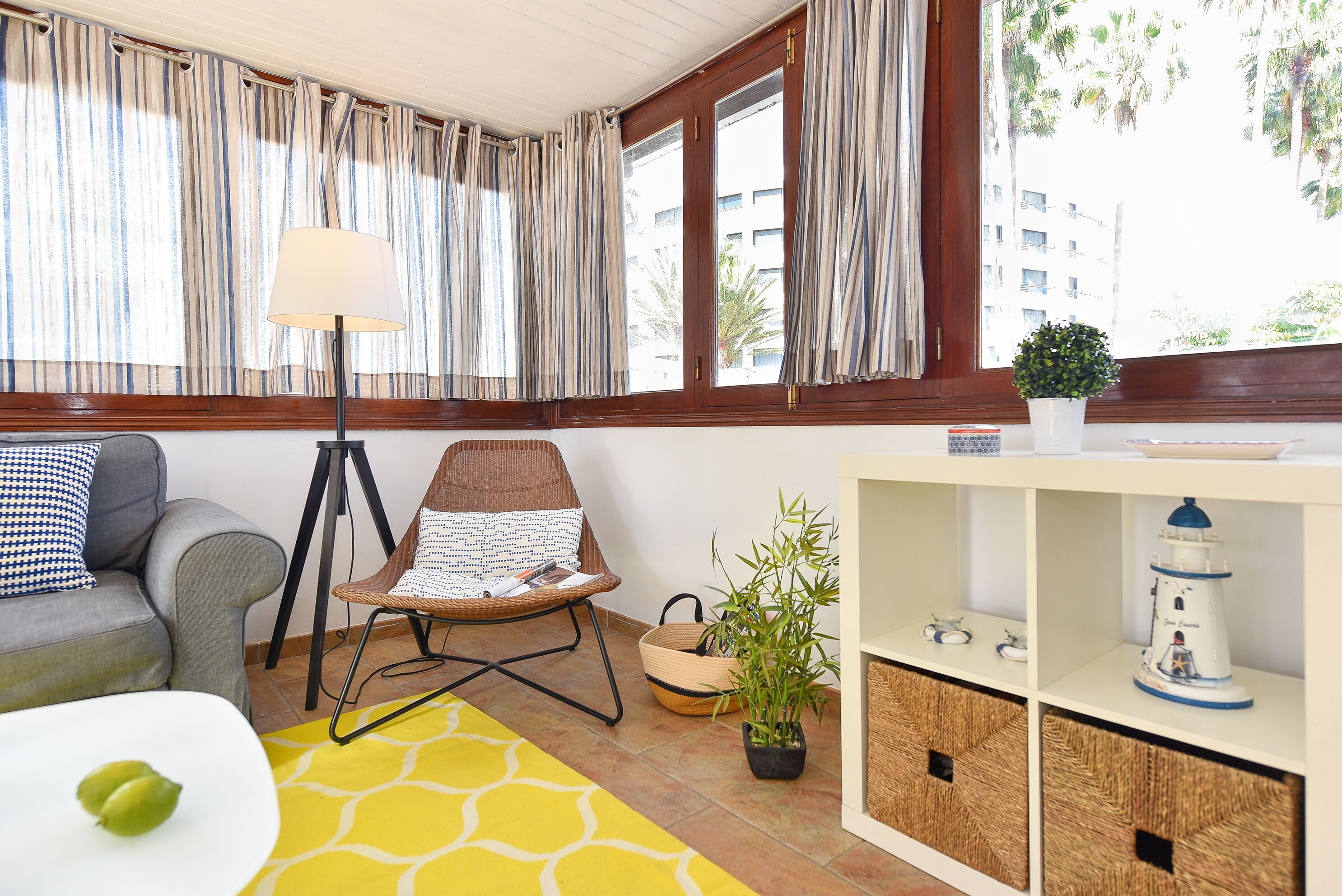 A living room with a sofa, a chair, a lamp, a potted plant, and a shelf with decorative items.