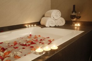 A bathtub with rose petals and candles, a stack of white towels, and a bottle of wine on the side. - Herald Suites Polaris (Makati)