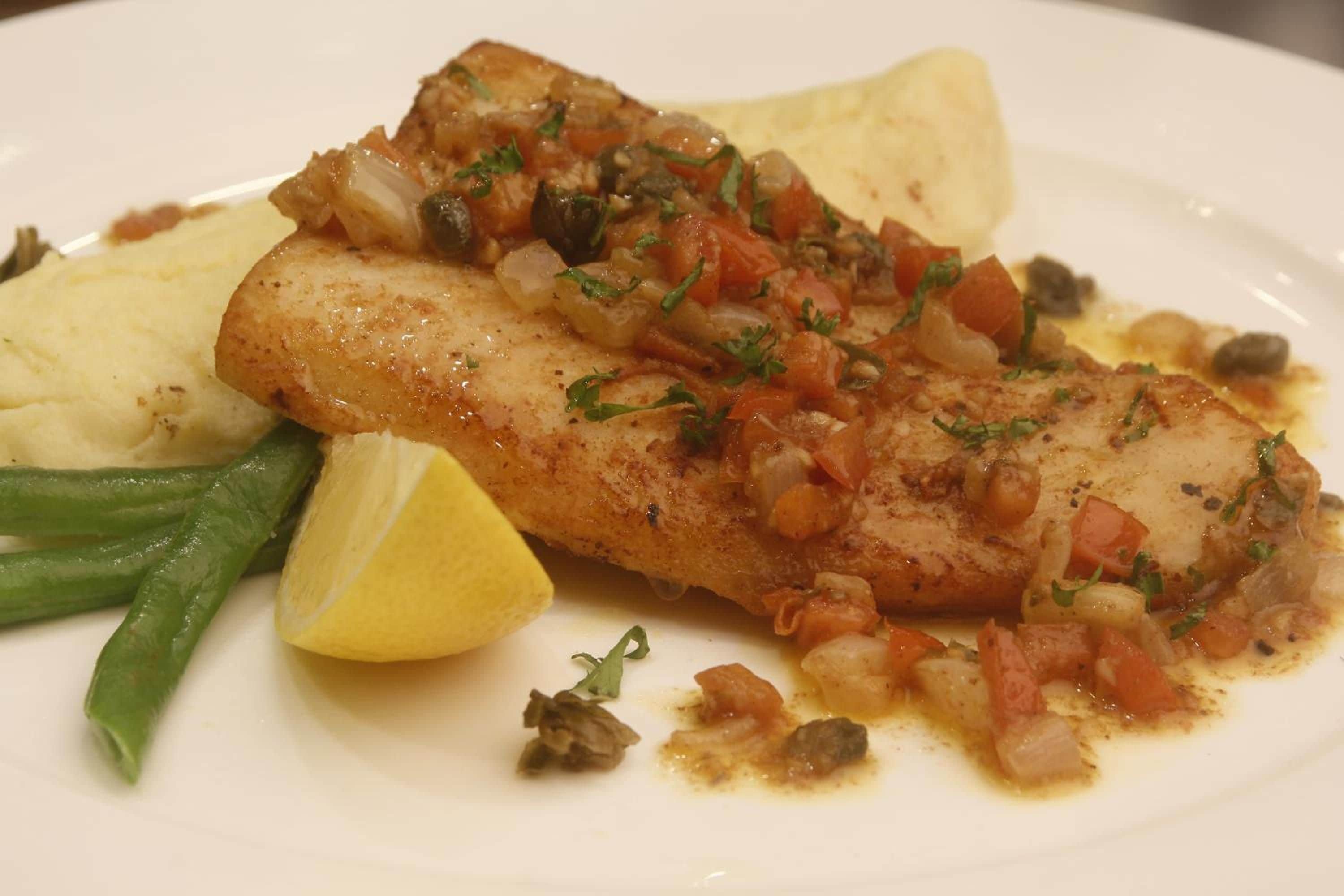 A plate with a fish fillet, mashed potatoes, green beans, and a lemon wedge.
