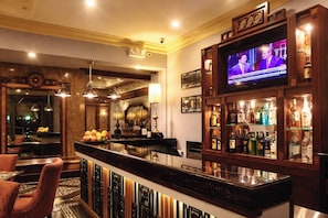 A bar area with a television displaying a news program, a variety of liquor bottles, and a seating area with chairs and a fruit bowl. - Herald Suites Polaris (Makati)