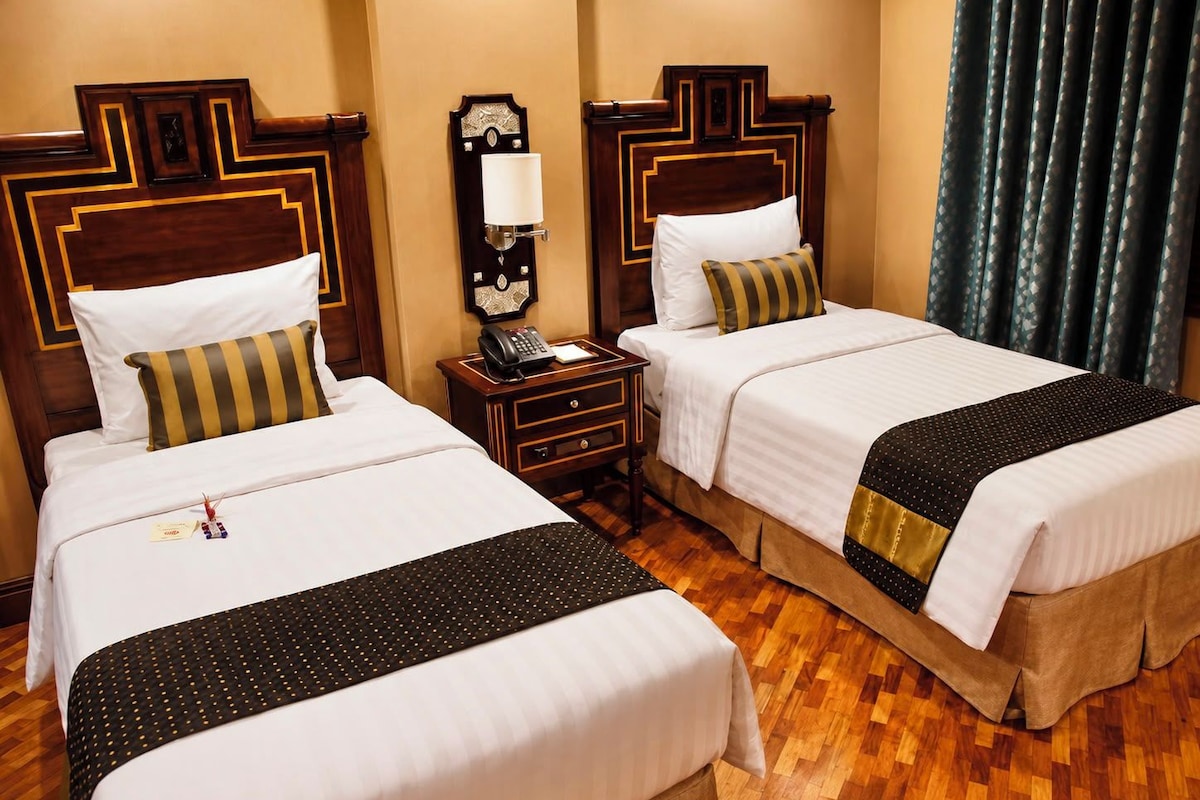 A hotel room with two beds, a nightstand with a telephone, and a wall-mounted lamp.