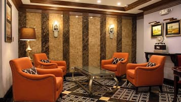 Un hall de hotel con piso a cuadros, sillones de cuero, una mesa de centro de vidrio y apliques de pared.