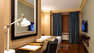 A hotel room with a bed, a desk with a lamp, a television, and a large mirror.