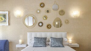 A hotel room with a bed, two nightstands, a chair, and wall decor including mirrors and sunburst patterns.