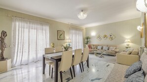 A spacious living room with a dining area, featuring a marble floor, a sofa set, and a chandelier.