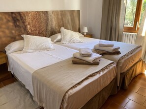 Een hotelkamer met twee bedden, elk voorzien van witte lakens en een beige plaid. Er staat een nachtkastje met een lamp en een raam met gordijnen.