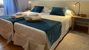 Uma cama de casal com duas almofadas, uma mesa de cabeceira com abajur e uma janela com cortinas.