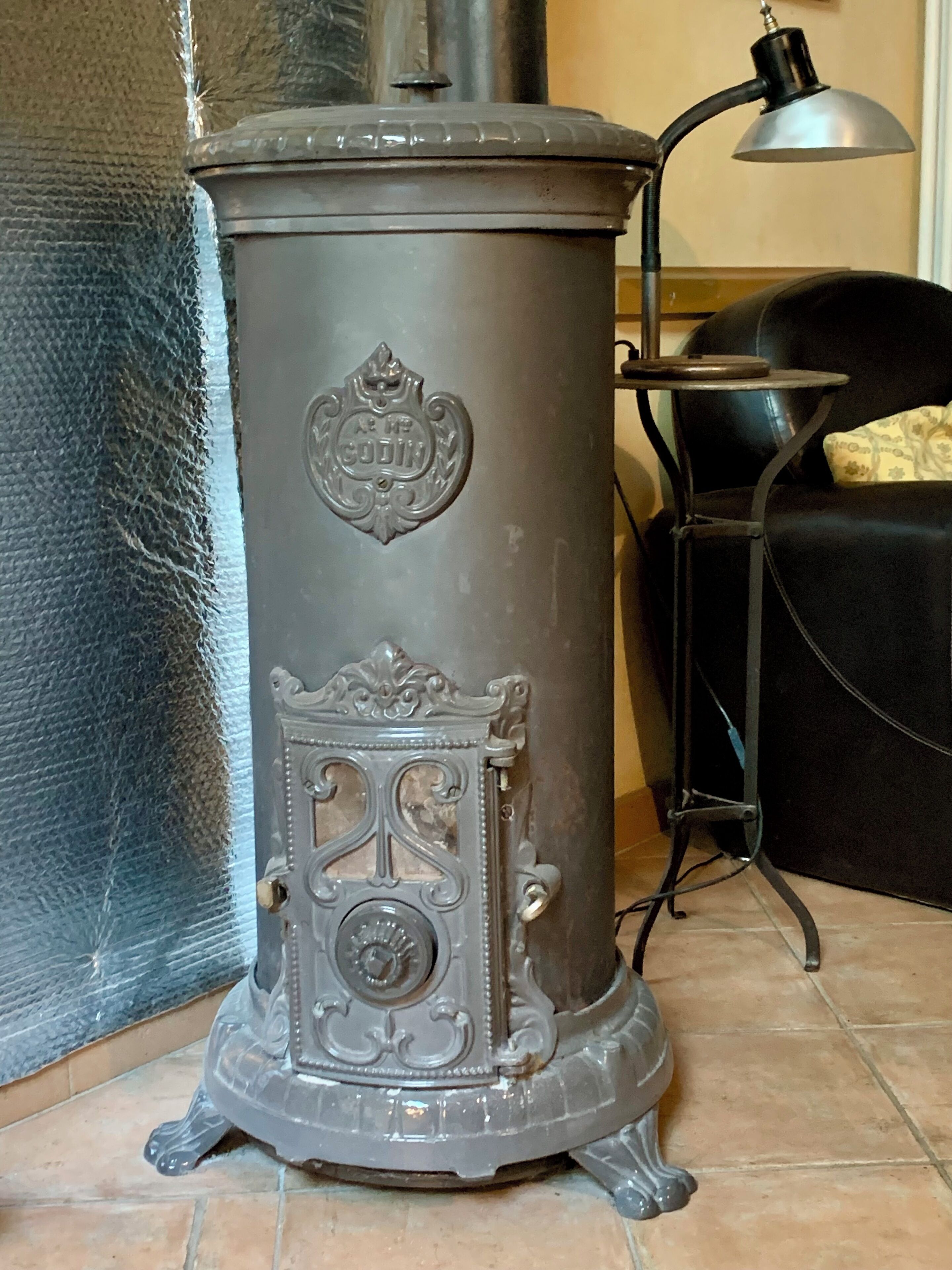 Una estufa antigua con detalles metálicos ornamentados y un emblema decorativo, sobre un piso de baldosas.