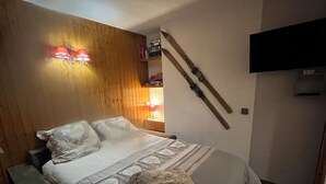 A bedroom with a wooden headboard, a bed with white bedding, a fluffy pillow, and a TV mounted on the wall. -  Les Coches / Plagne Tarentaise resort center comfortable apartment 4/5 people (La Plagne Tarentaise)