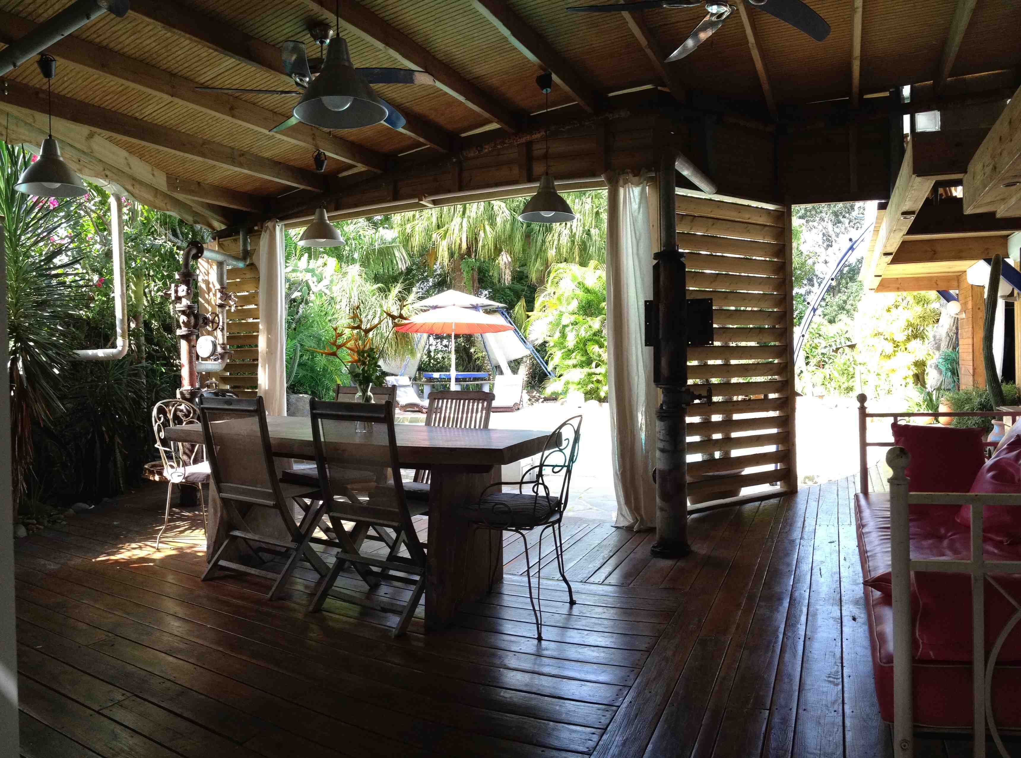 Een houten terras buiten met een tafel en stoelen, omgeven door weelderige begroeiing.