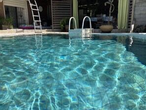 A clear pool with a ladder and two steps leading into it.