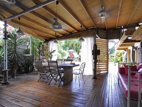An outdoor covered patio with wooden flooring, a table with chairs, and a red sofa.